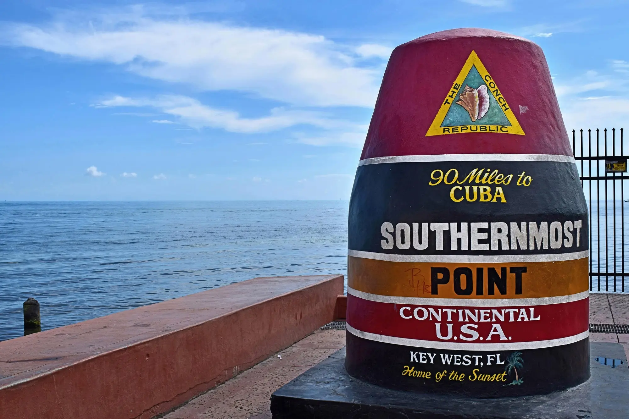 The Southernmost Point buoy in Key West, painted red, black and yellow, beside the water